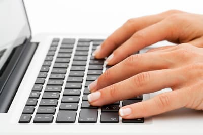 Frauenhände bedienen eine Laptop-Tastatur.