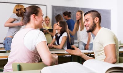 Zwei Studierende unterhalten sich angeregt im Klassenzimmer.