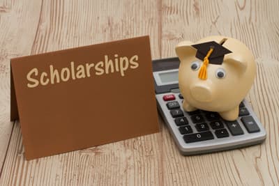 Sparschwein mit Doktorhut auf einem Taschenrechner neben einem Schild mit der Aufschrift "Scholarships"