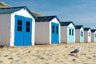 weiße Holzhäuser mit blauen Türen am Strand