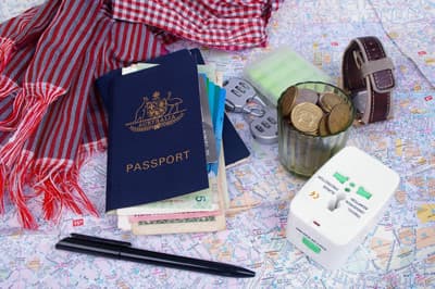 Reiseunterlagen wie Reisepass, Geldmünzen, Reiseadapter und Kofferschloss auf einer Karte