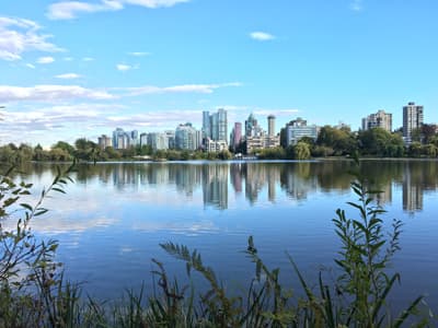 Ein See mit viel grün und der Skyline von Vancouver im Hintergrund