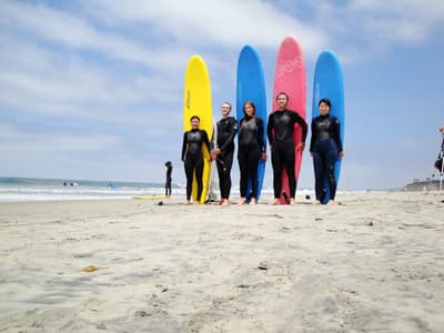 Fünf Studenten vor bunten Surfbrettern in Wetsuits am Strand