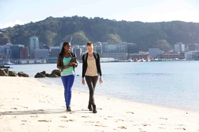 zwei Frauen spazieren einen städtischen Strand entlang und unterhalten sich