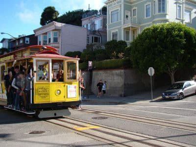 Fahre mit einem der berühmten Cable Cars von San Francisco Gelbes Cable Car, das an wohlhabend aussehenden Häusern vorbeifährt